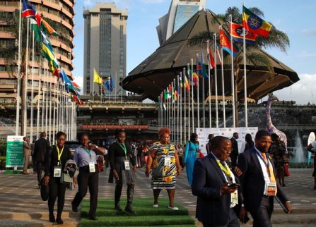 Delegates with conference badges walking outside a convention centre lined with African national flags